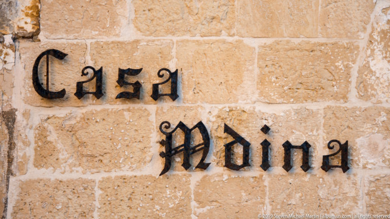 Black metal letters spelling Casa Mdina mounted on rough honey-colored limestone blocks.