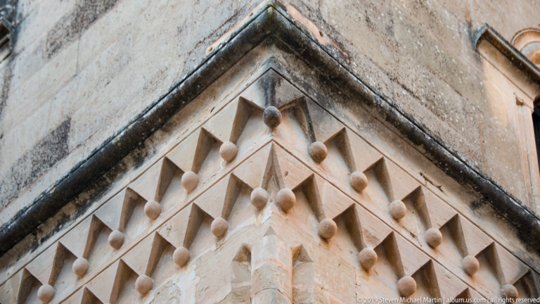 Close view of a limestone building corner decorated with rows of projecting pyramidal stone bosses.