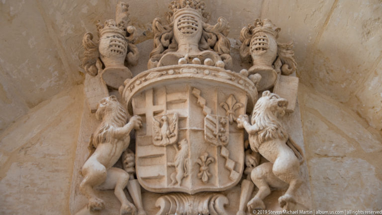 Carved stone coat of arms with quartered shield, two rampant lion supporters, and figures above.