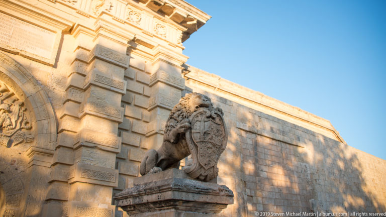 Stone lion holding a heraldic shield beside the rusticated masonry of Mdina Gate.