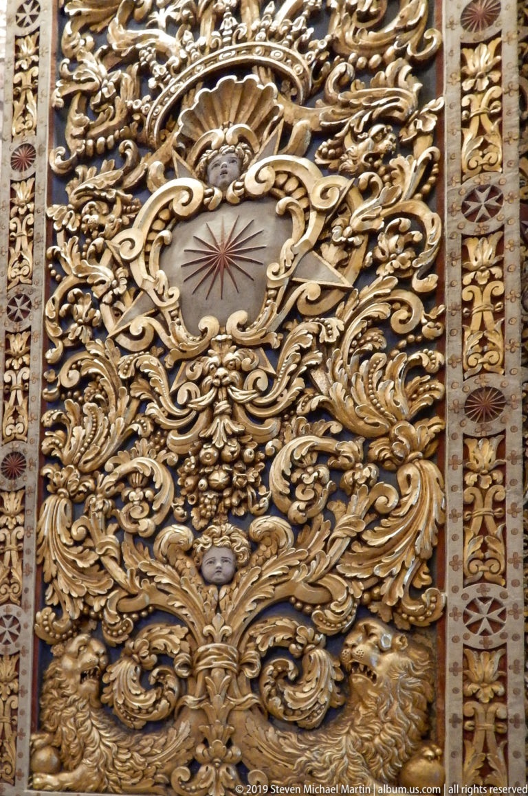 Close view of dense gilded scrolling relief around a pale central cartouche with a small radiating star motif.