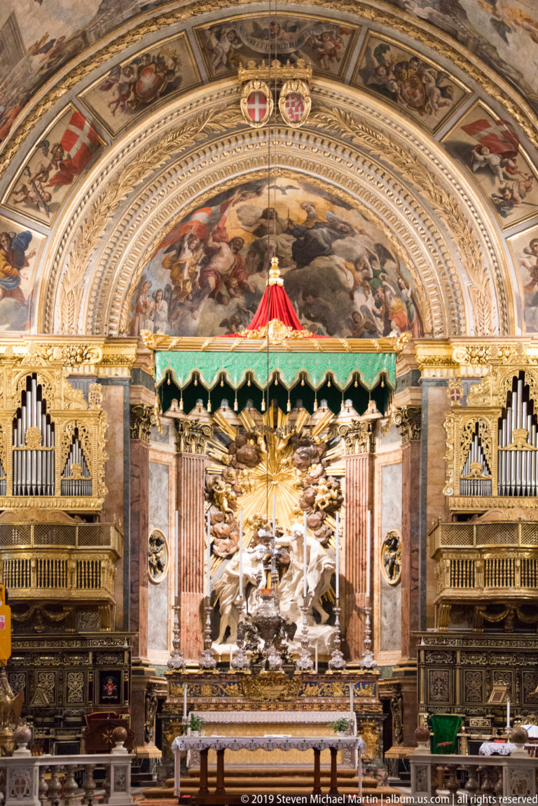 Frontal view of the sanctuary with central altar, green-and-red canopy, paired organ cases, and a painted arch above.