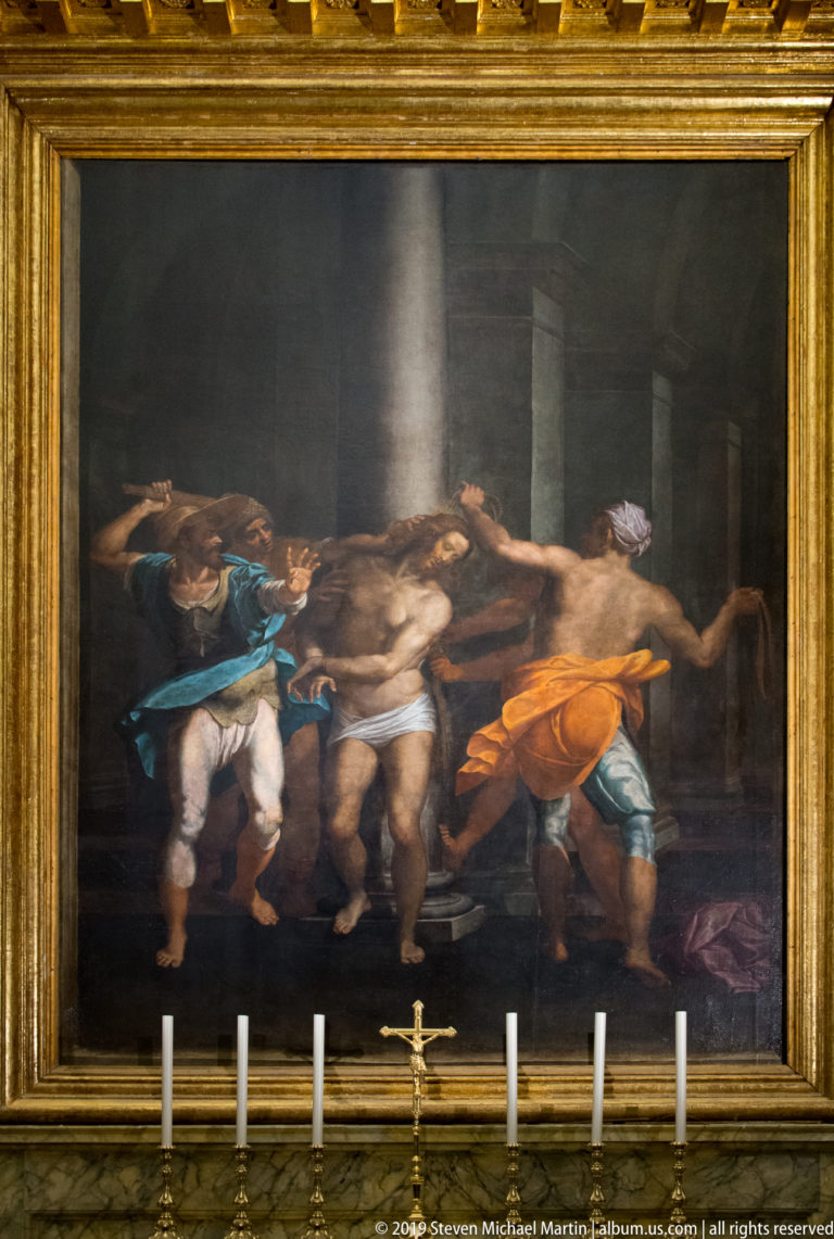 Dark religious canvas with several figures, broad gilded frame, and altar candles visible along the lower edge.