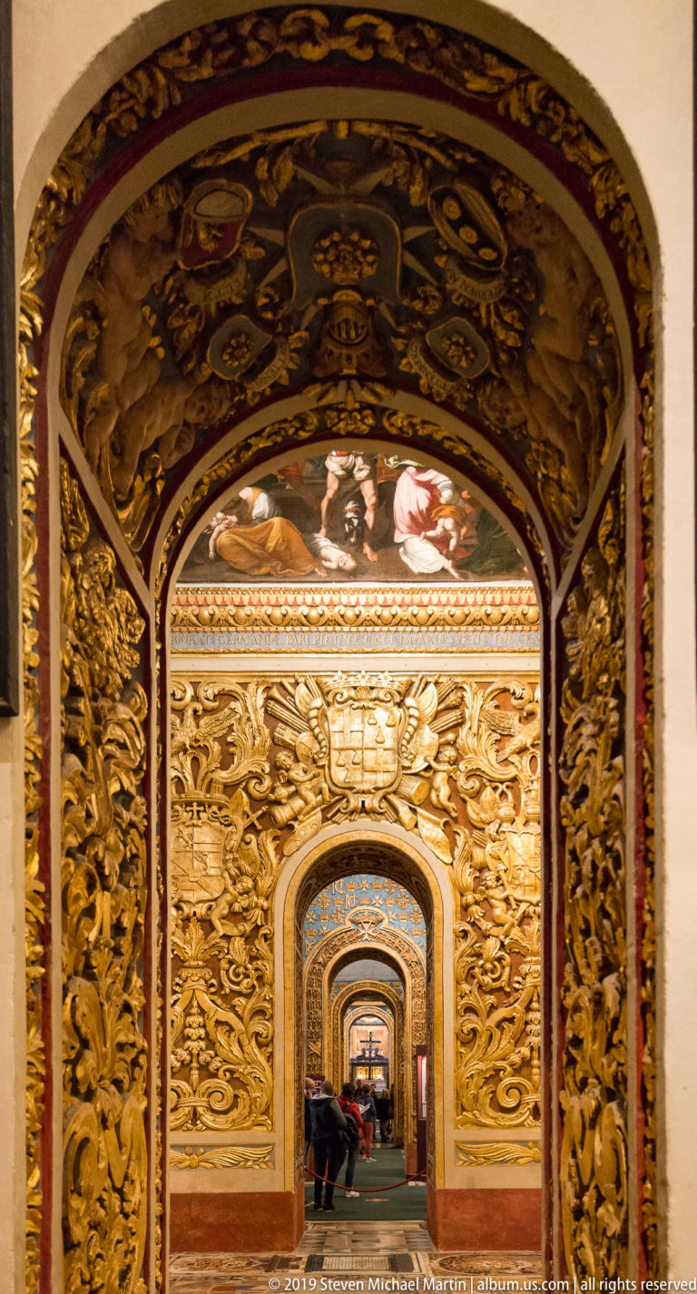 Nested arched openings receding through richly gilded chapel walls with dense relief foliage and dark painted framing.