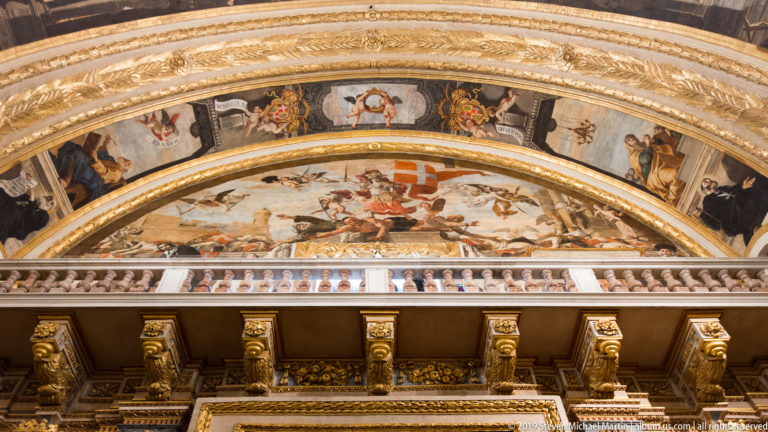 Painted lunette above a projecting gilded cornice with brackets, moldings, and balustrade-like detailing.