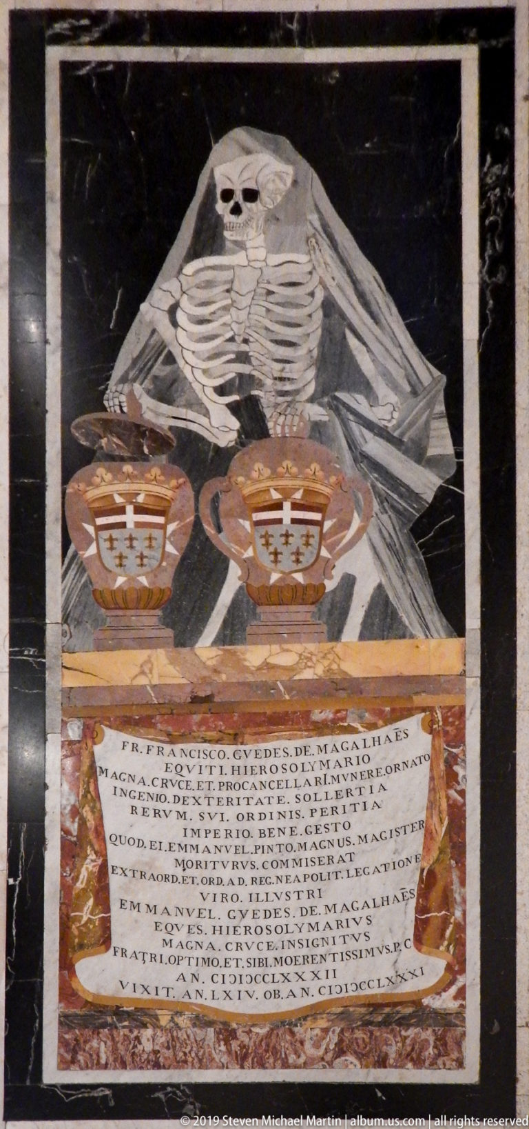 Inlaid marble tomb slab with shrouded skeleton, two heraldic shields, and a large Latin inscription.