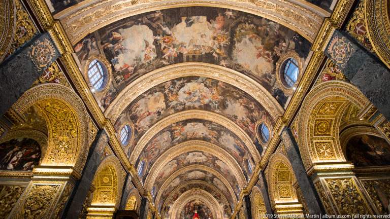 Upward axial view of the nave’s frescoed barrel vault, gilded ribs, oval windows, and richly ornamented arches.