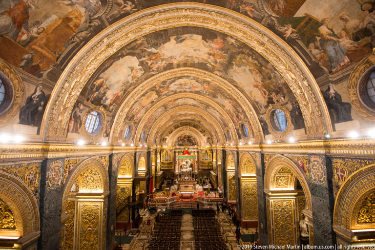 Upward view along the nave’s frescoed barrel vault with oval windows, gilded ribs, and ornamented arches.