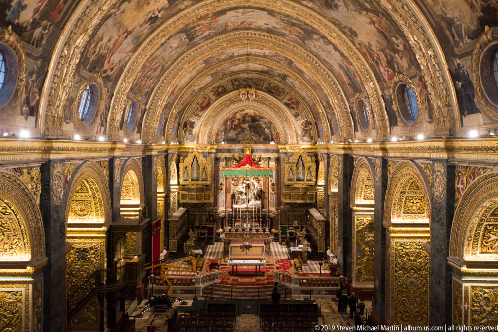 Centered elevated view down the nave toward the sanctuary beneath richly painted and gilded vaulting.