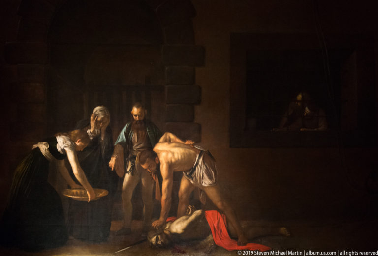 Dark religious painting with several figures gathered around a brightly lit, nearly nude figure in an interior.