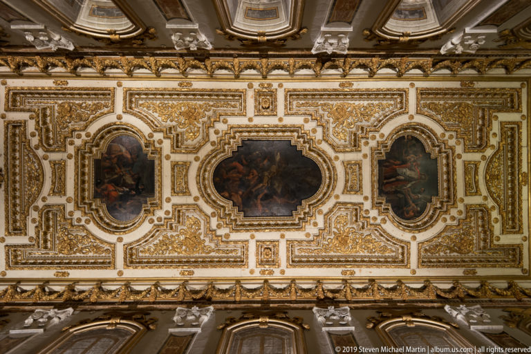 Three ceiling paintings framed by elaborate white-and-gold moldings and dense gilded foliate ornament.