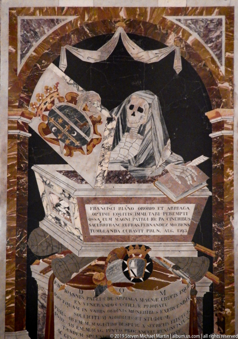 Inlaid marble tomb slab with a shrouded skeleton, heraldic arms, funerary emblems, and multiple inscribed panels.