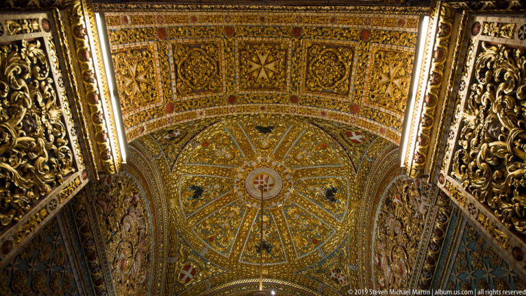 Gilded and blue vaulted ceiling with radial bay, rectangular coffers, Maltese crosses, and other heraldic cross motifs.