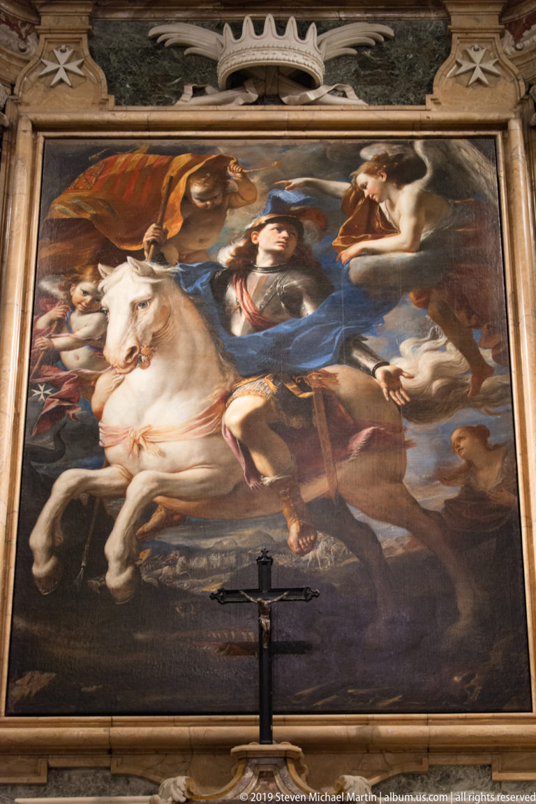 Large framed painting of a mounted figure on a white horse amid other figures, with a crucifix standing below.
