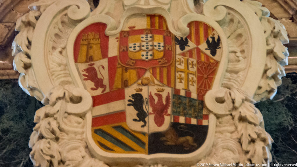 Multi-field polychrome coat of arms with castles, lions, crosses, eagles, and stripes in a white sculpted cartouche.