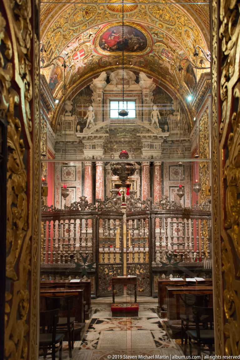Side chapel with marble altar wall, balustrade, patterned floor, painted ceiling, and polychrome architectural panels.