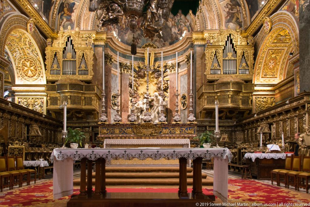 High altar centered between paired organ cases and choir stalls beneath richly gilded and painted vaulting.