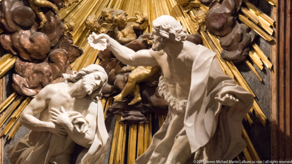 Close view of Christ bowing beside John the Baptist, with angels, clouds, and gilded rays behind them.