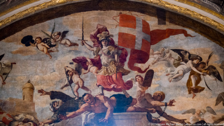 Painted vault scene with armored figure holding a red-and-white cross banner, surrounded by putti and other figures.