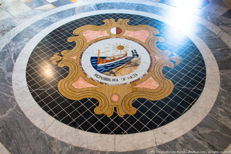 Circular marble floor inlay with the Republic of Malta emblem, decorative cartouche, and inscription “REPUBBLIKA TA’ MALTA.”