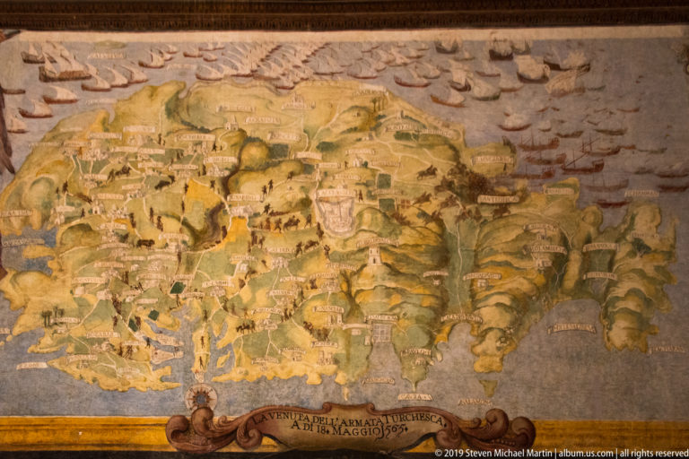 Historic painted bird’s-eye map of Malta showing settlements, roads, hills, fortified places, surrounding sea, and numerous small ships.