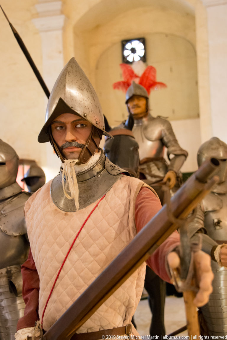Armored soldier mannequin holding a long weapon, with several helmeted figures and a red-plumed soldier displayed behind.