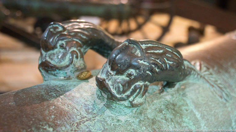 Close view of two small animal-head fittings projecting from green-patinated metal, with rounded muzzles and worn sculpted features.