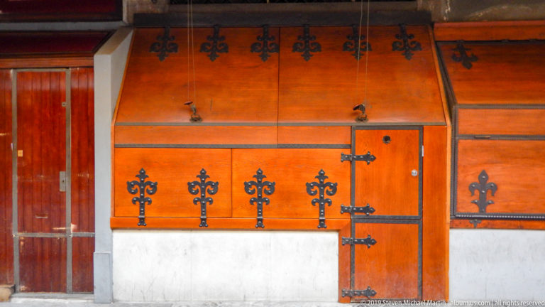 Closed varnished wooden Ponte Vecchio shopfront with black iron hinges, straps, latches, and decorative fittings above a stone base.