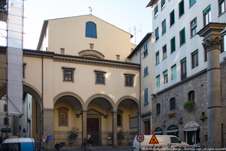 Small Florentine church with three-arched portico, slender columns, central doorway, tall upper window, and a small roof cross.