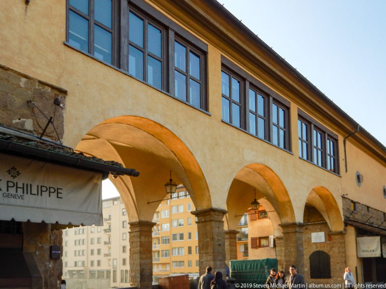 Three ochre arches on heavy stone piers beneath a row of upper windows near the Ponte Vecchio approach.