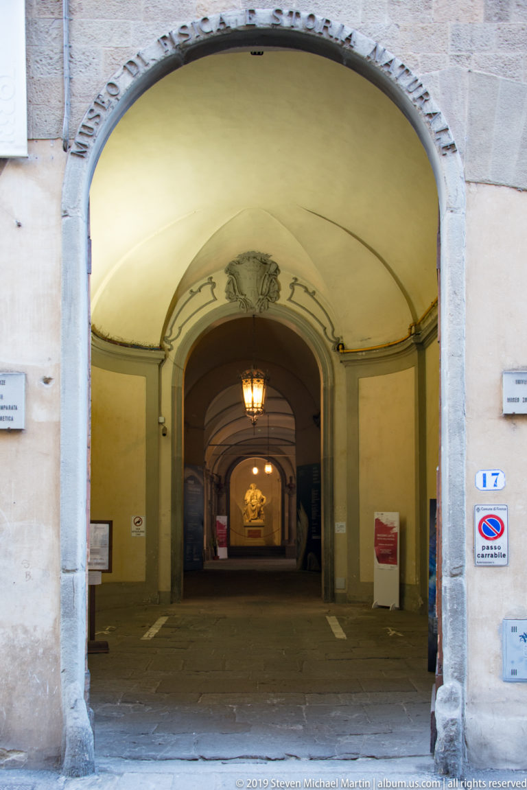 Large stone-framed arch opening into a yellow vaulted passage with hanging lanterns and successive arches receding into the distance.