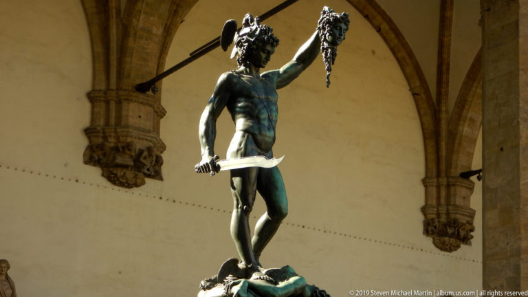 Low-angle view of bronze Perseus raising Medusa’s severed head and holding a curved sword beneath the Loggia dei Lanzi.