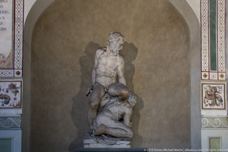 Marble group of a muscular standing man overpowering a kneeling figure inside an arched niche in Palazzo Vecchio.
