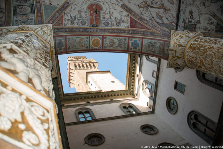 Upward view through Palazzo Vecchio’s decorated courtyard toward blue sky and the upper Torre di Arnolfo.