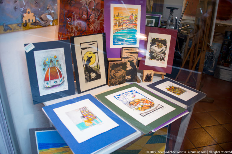 Shop window filled with colorful Florence-themed prints and small artworks arranged on tables and upright display boards.