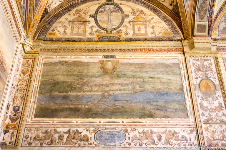 Large rectangular landscape fresco surrounded by grotesque ornament, medallions, inscriptions, and painted architectural borders.