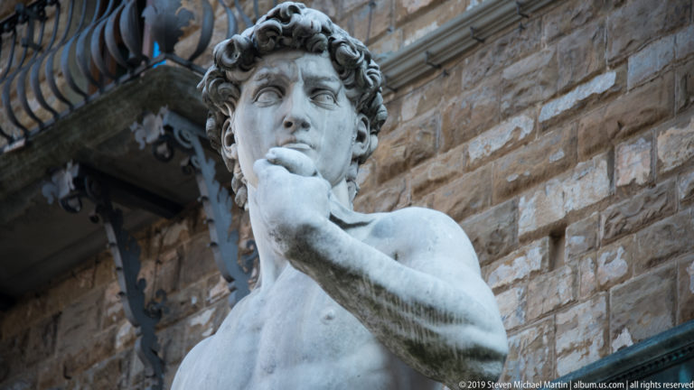 Close view of the David replica’s head, torso, and raised hand against the rusticated wall of Palazzo Vecchio.