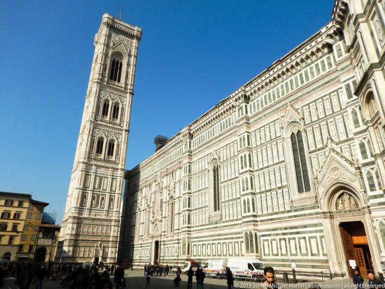 Giotto’s Campanile beside the richly patterned marble flank of Florence Cathedral under a clear blue sky.