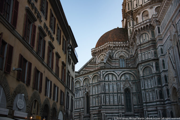 Florence Baptistery’s polychrome marble exterior seen from a narrow street, with Brunelleschi’s dome rising behind.