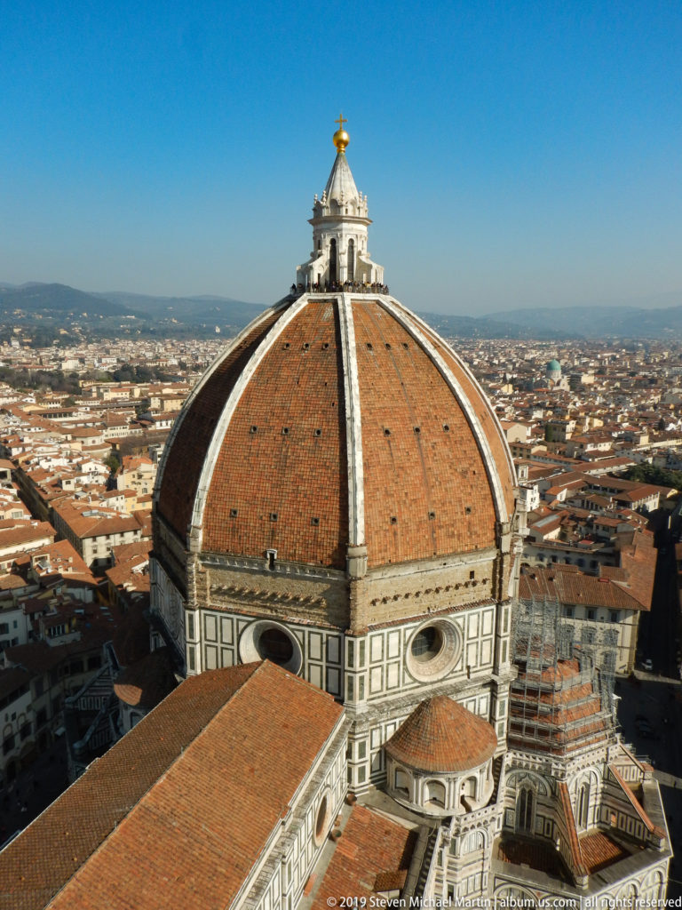 Close elevated view of Brunelleschi’s terracotta dome, stone ribs, marble drum, and lantern above Florence.