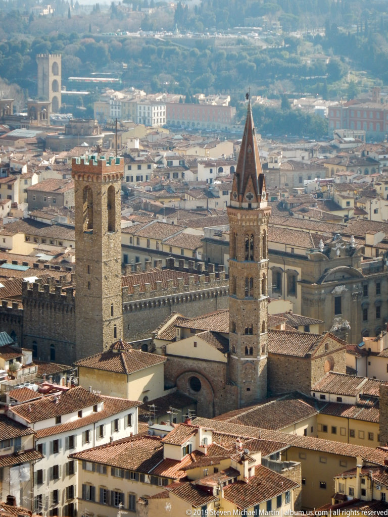 Elevated view of the pointed Badia Fiorentina campanile and heavier Bargello tower among central Florence rooftops.