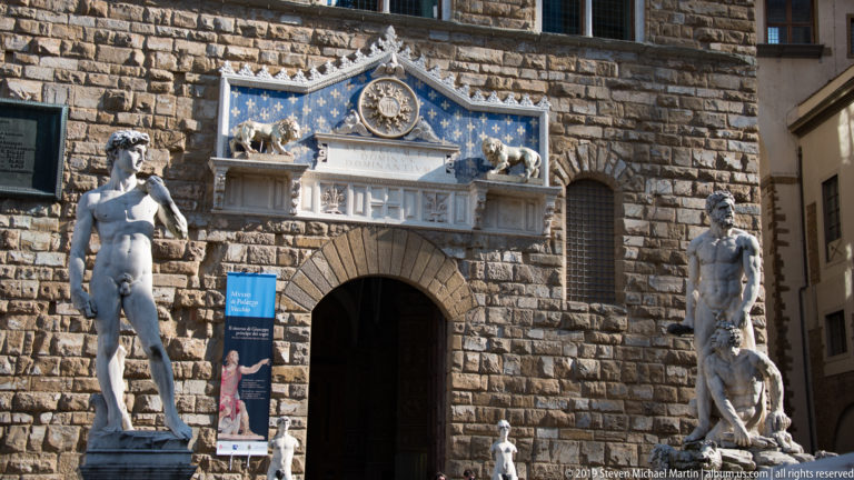 Palazzo Vecchio entrance between the David replica and Hercules and Cacus, beneath a blue-and-gold decorated portal.