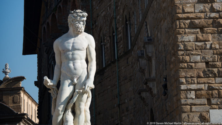 Side view of the marble Hercules and Cacus group, with muscular Hercules holding a club beside Palazzo Vecchio.