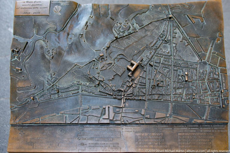 Bronze tactile relief map of central Florence showing the Arno, street network, buildings, markers, and explanatory panels.