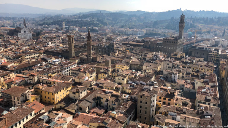 Elevated panorama of central Florence with Palazzo Vecchio and the Torre di Arnolfo rising above dense terracotta rooftops.
