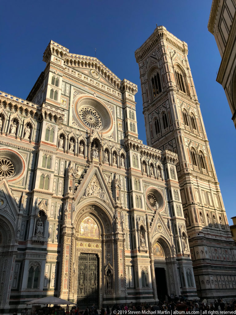 Low-angle view of Florence Cathedral’s polychrome marble façade beside Giotto’s Campanile under a deep blue sky.