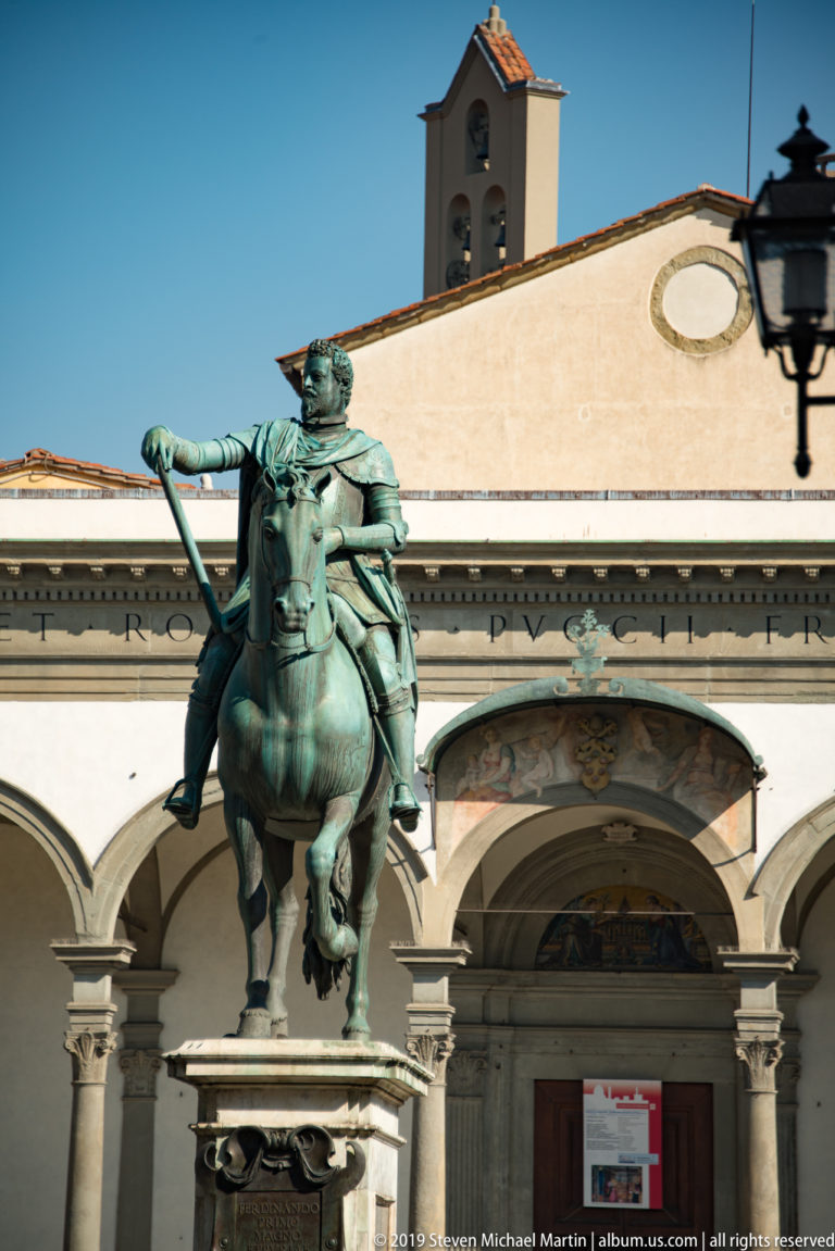 Bronze equestrian statue of mounted man holding a baton before Santissima Annunziata's arcaded portico.