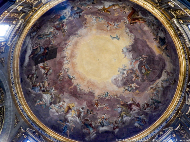 Full circular dome fresco with luminous center, clouds, angels, sacred figures, gilded border, and inscription band.