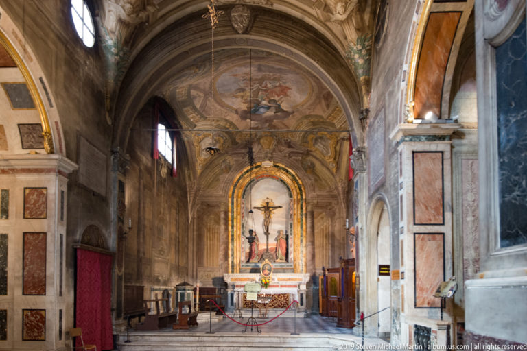Long view into a side chapel toward a Crucifixion altar beneath a painted barrel vault.