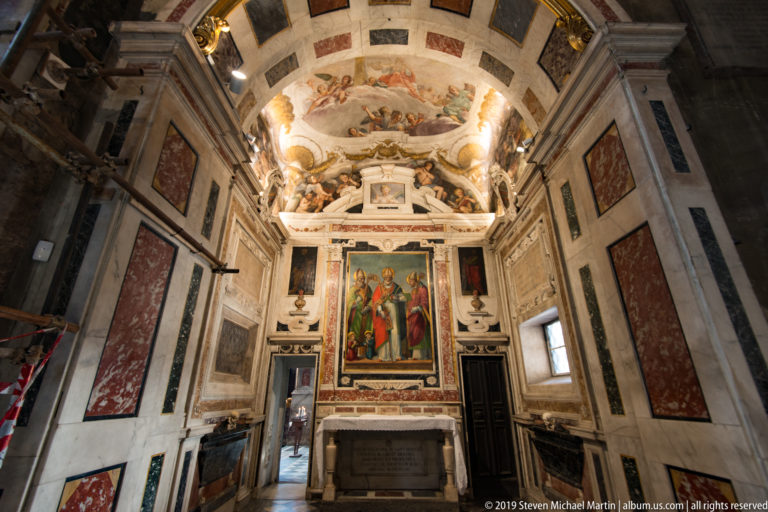Marble-lined side chapel with large painted altarpiece, frescoed vault, colored wall panels, and altar table.